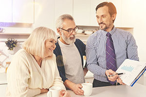 Examine prices. Cheerful professional  agent presenting graph and meeting with smiling aged couple at home